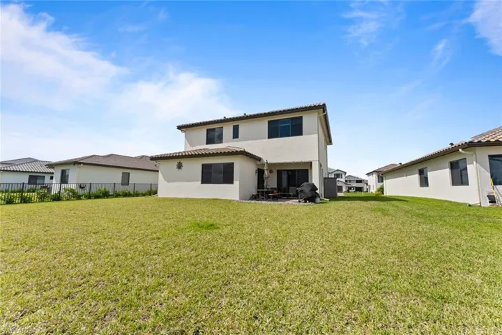 Back of house with a lawn, a tile roof, fence, and stucco siding