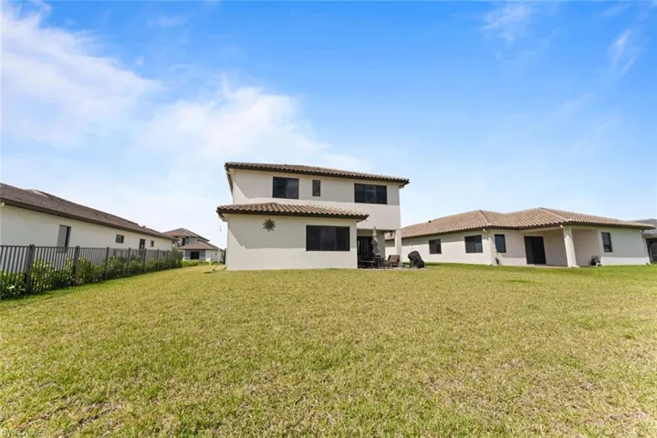 Back of house with a tile roof, stucco siding, a lawn, and fence