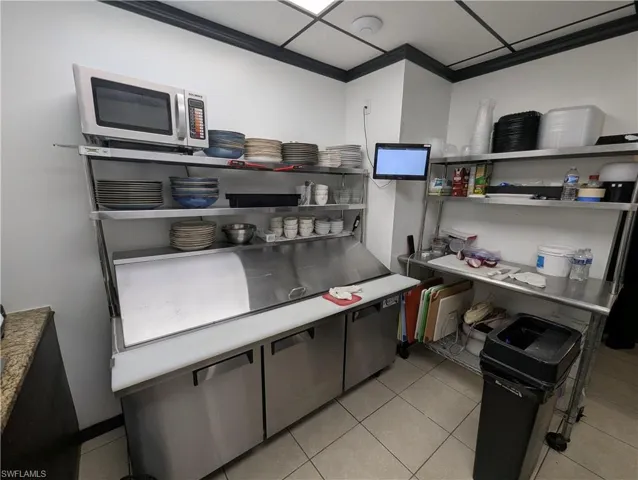 Stainless steel commercial kitchen setup featuring a three-door under-counter refrigerator with a prep station, multiple open shelving units, and a mounted microwave