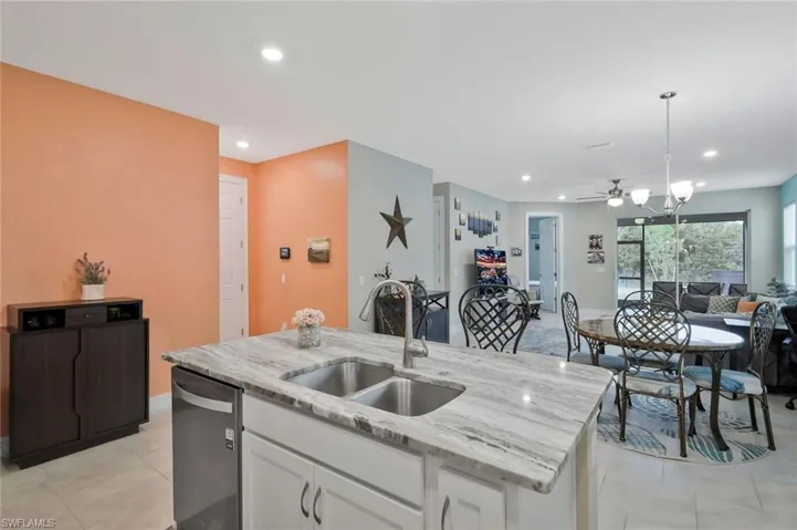 Kitchen with white cabinets, light stone counters, open floor plan, an island with sink, and recessed lighting