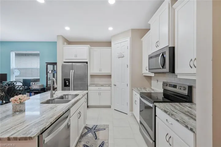 Kitchen featuring appliances with stainless steel finishes, white cabinetry, light stone countertops, a kitchen island with sink, and recessed lighting