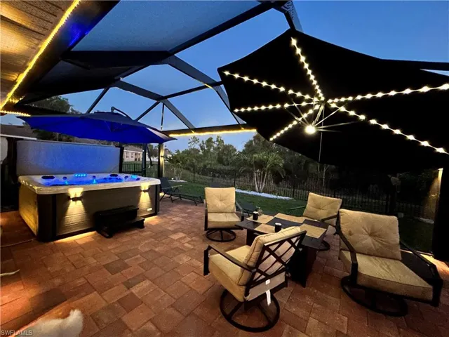 Screened-in patio featuring brick paver flooring, a built-in hot tub, and overhead string lighting