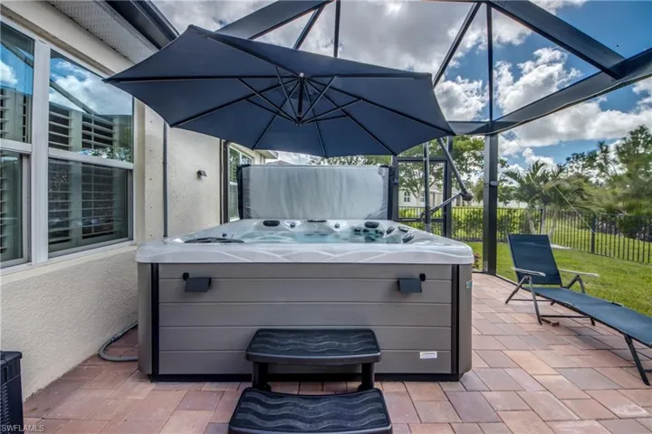 Expansive paver patio with a built-in hot tub, screened enclosure, and privacy fencing
