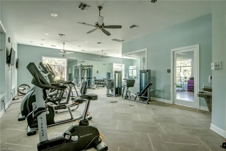 Spacious fitness area featuring carpeted flooring, multiple ceiling fans, large windows, and a mirrored wall
