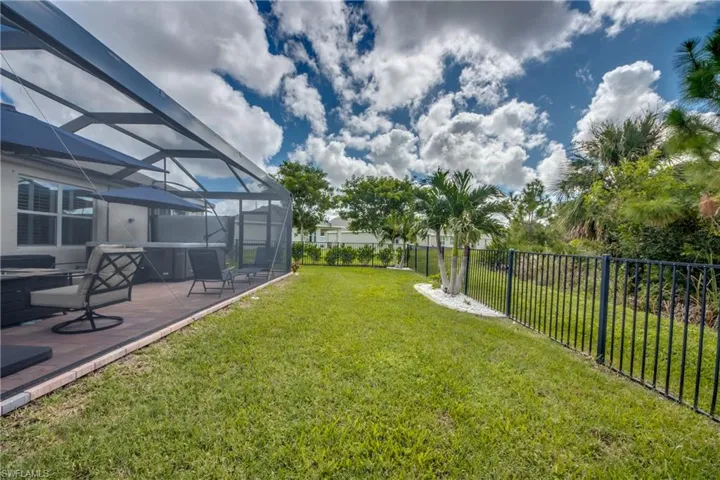 Screened patio enclosure with a hot tub and tiled flooring, featuring a manicured lawn and a black metal fence