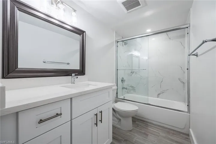 Full bathroom with vanity, toilet, wood finished floors, combined bath / shower with glass door, and recessed lighting