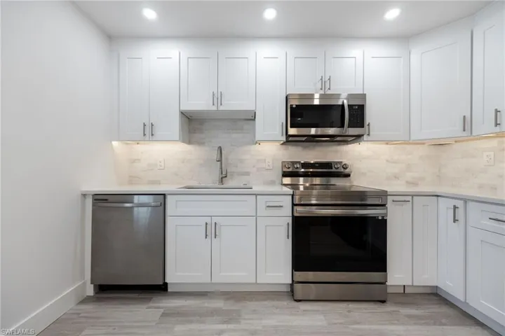 Kitchen with appliances with stainless steel finishes, a sink, light countertops, tasteful backsplash, and recessed lighting