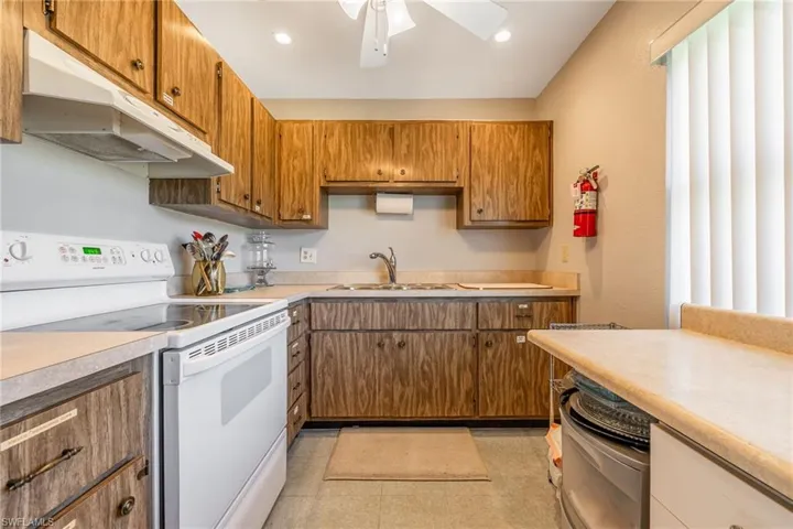 Kitchen featuring white range with electric cooktop, a sink, under cabinet range hood, light countertops, and recessed lighting
