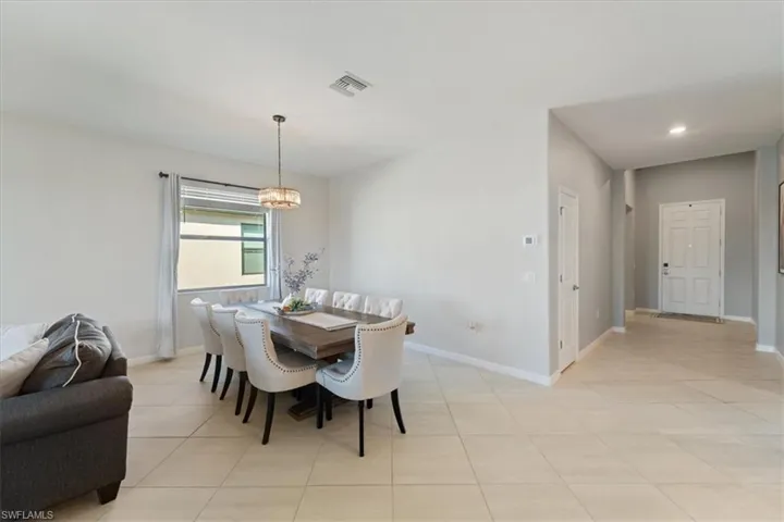 Spacious open-concept area featuring light-toned tile flooring, recessed lighting, and a modern chandelier
