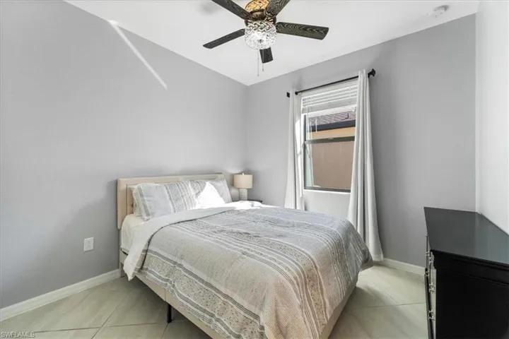 Light gray interior walls with a single window, a dark wood-finish ceiling fan with a decorative light fixture, and light-toned tile flooring