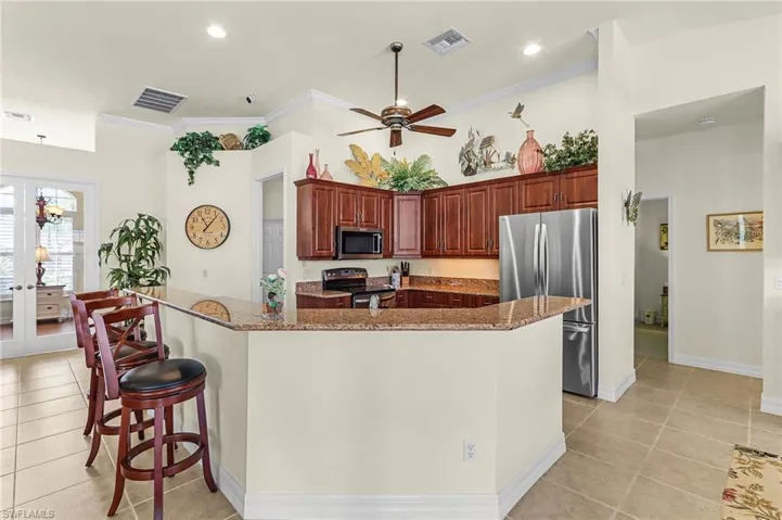 Kitchen with stainless steel appliances, light tile patterned flooring, a large island with sink, french doors, and ornamental molding