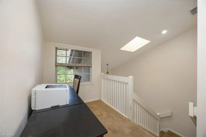 Carpeted office featuring vaulted ceiling with skylight, visible vents, and a sink