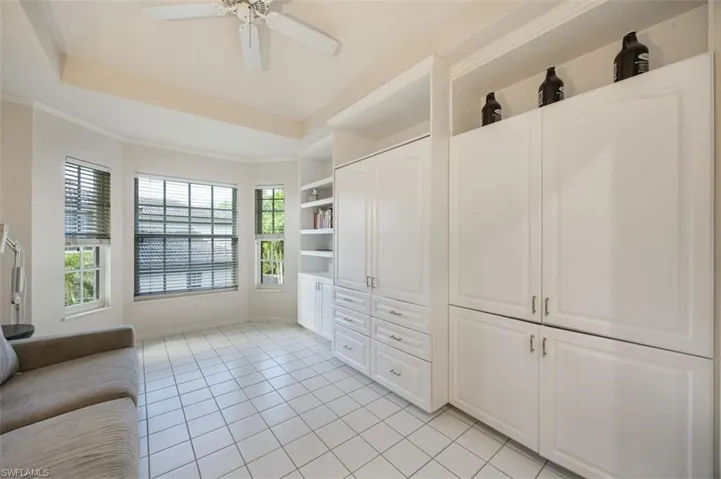 Spacious den featuring a tray ceiling, light tile patterned floors, and ceiling fan