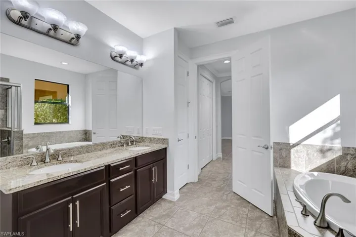 Bathroom featuring tiled tub, vanity, and tile patterned floors