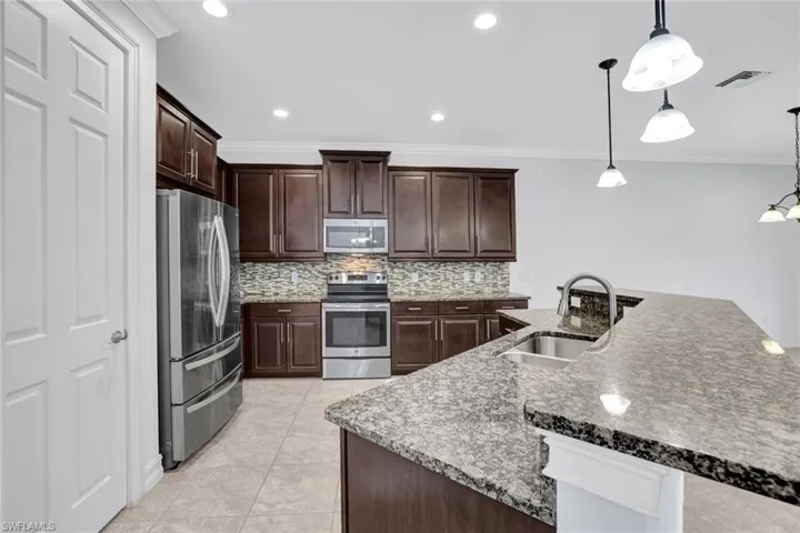 Kitchen with sink, light tile patterned floors, ornamental molding, appliances with stainless steel finishes, and pendant lighting