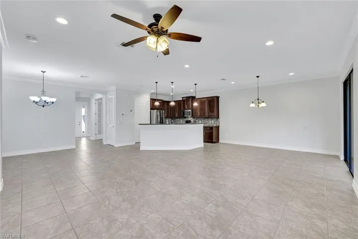 Unfurnished living room featuring crown molding, ceiling fan with notable chandelier, and light tile patterned floors