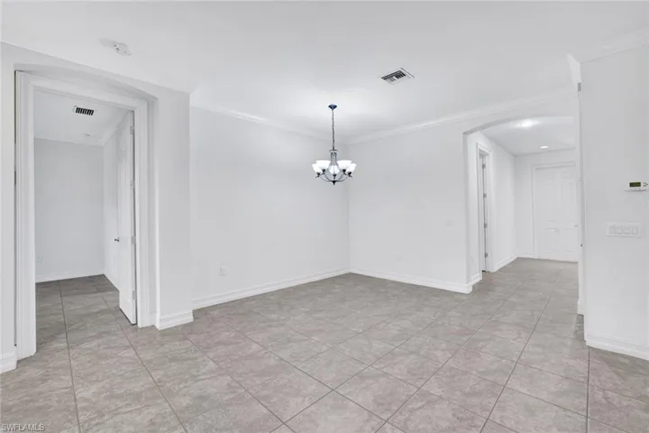Spare room featuring ornamental molding, light tile patterned floors, and a notable chandelier