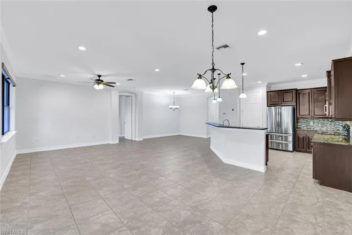 Kitchen featuring dark brown cabinetry, decorative light fixtures, stainless steel fridge, dark stone counters, and decorative backsplash