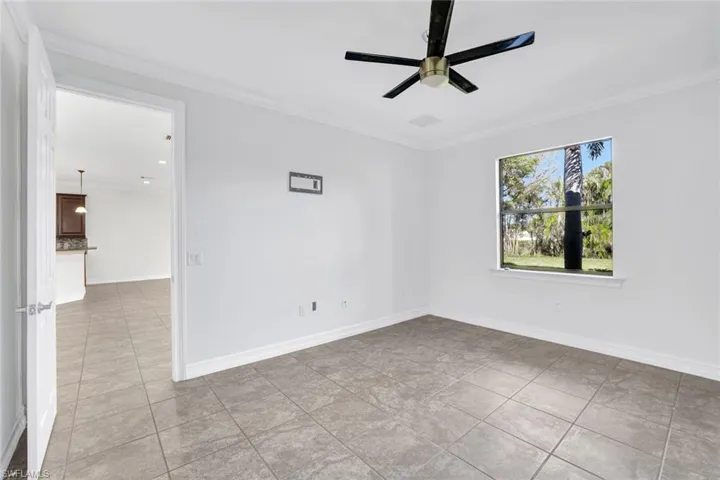 Empty room featuring crown molding, light tile patterned floors, and ceiling fan