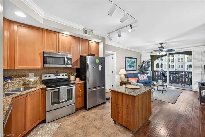 Kitchen featuring crown molding, wood finish cabinets, stainless steel appliances, light stone counters, and track lighting