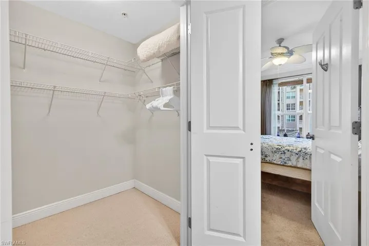 Walk in closet with a ceiling fan and light carpet