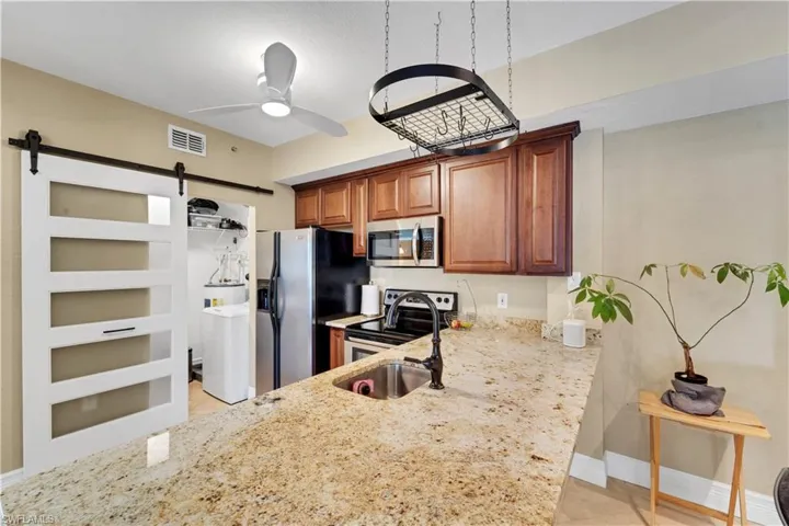 Kitchen featuring light stone counters, appliances with stainless steel finishes, a barn door, washer / dryer, and light tile patterned flooring
