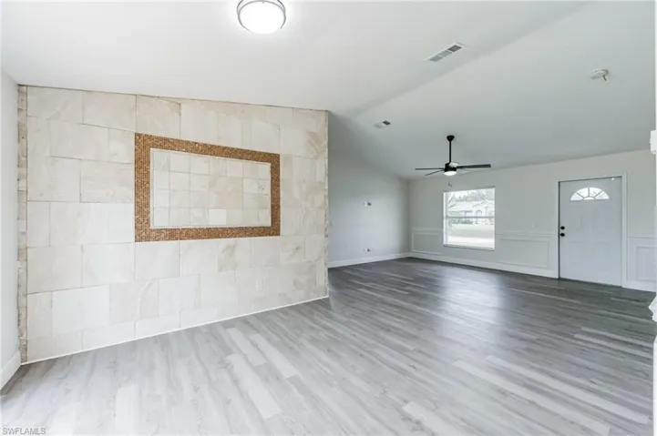 Unfurnished living room featuring vaulted ceiling, ceiling fan, tile walls, and hardwood / wood-style flooring