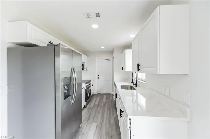 Kitchen with stainless steel appliances, white cabinets, sink, and light wood-type flooring