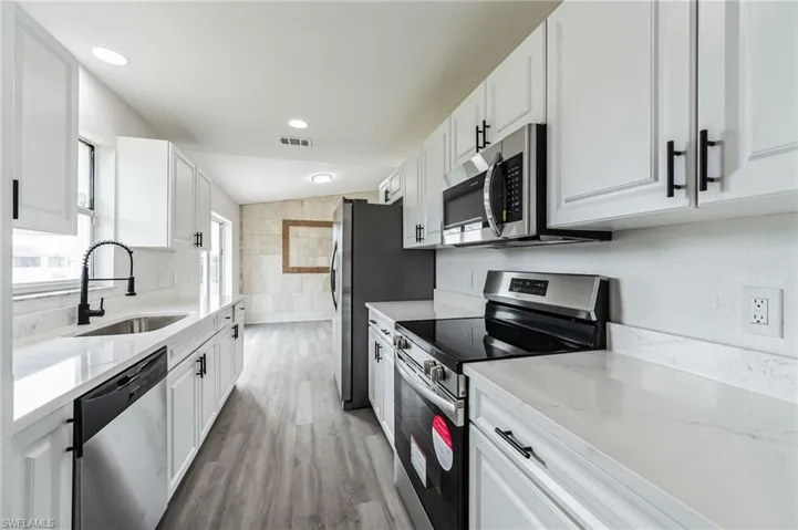 Kitchen featuring light hardwood / wood-style floors, white cabinetry, lofted ceiling, appliances with stainless steel finishes, and sink