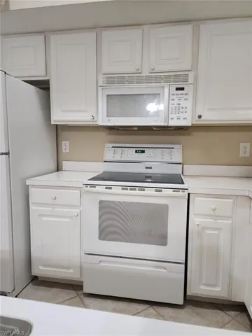 Kitchen featuring white appliances, light countertops, white cabinets, and light tile patterned flooring