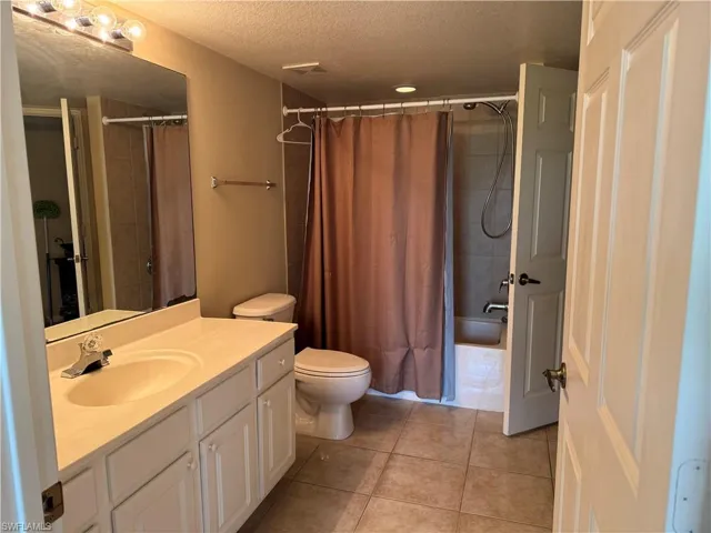 Full bathroom with vanity, a textured ceiling, light tile patterned floors, and shower / bath combo with shower curtain