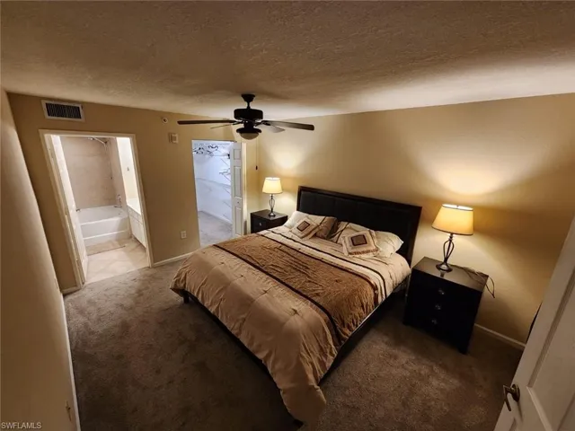 Bedroom with carpet floors, a textured ceiling, ensuite bath, a ceiling fan, and a walk in closet