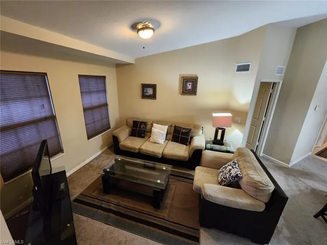 Living area with lofted ceiling and dark colored carpet