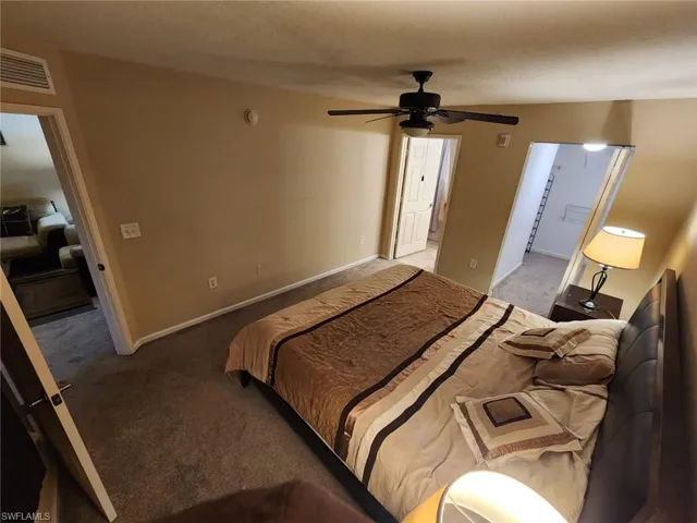 Bedroom with light colored carpet, connected bathroom, ceiling fan, and a textured ceiling