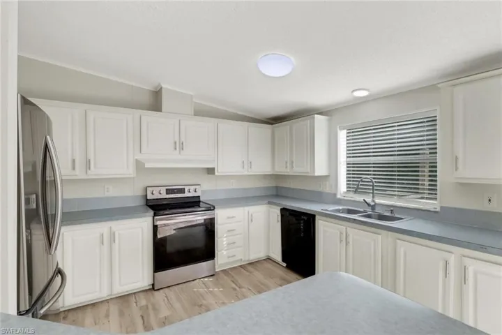Kitchen with white cabinetry, sink, stainless steel appliances, light hardwood / wood-style flooring, and lofted ceiling