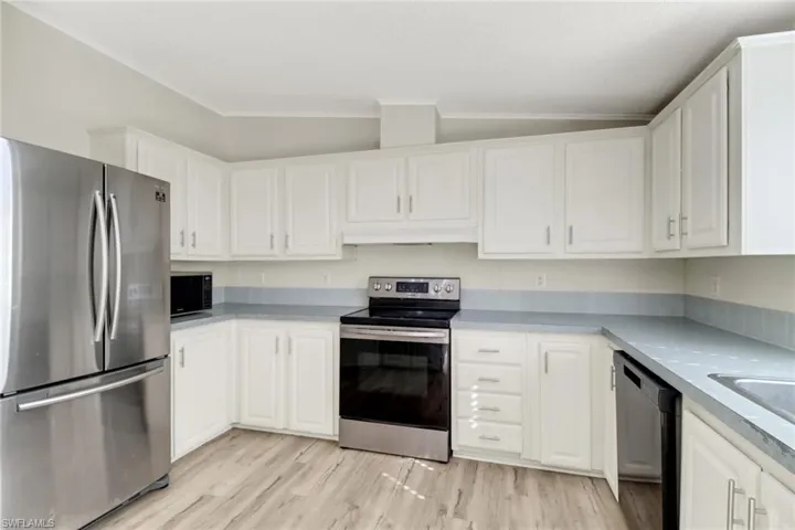 Kitchen with stainless steel appliances, vaulted ceiling, crown molding, white cabinets, and light hardwood / wood-style floors