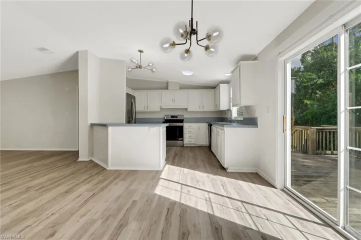 Kitchen with appliances with stainless steel finishes, vaulted ceiling, pendant lighting, a notable chandelier, and white cabinetry