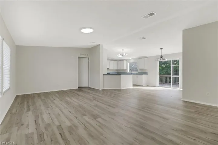 Unfurnished living room with light hardwood / wood-style floors, vaulted ceiling, and an inviting chandelier