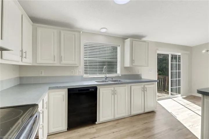 Kitchen with light hardwood / wood-style floors, sink, white cabinetry, and black dishwasher