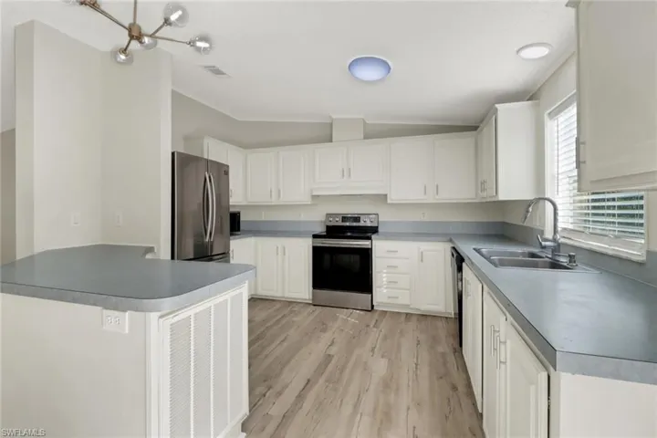 Kitchen featuring lofted ceiling, white cabinets, sink, light wood-type flooring, and appliances with stainless steel finishes