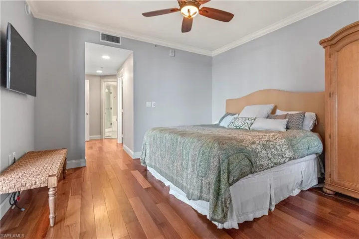 Primary bedroom with ornamental molding, teak floors, and ensuite bath