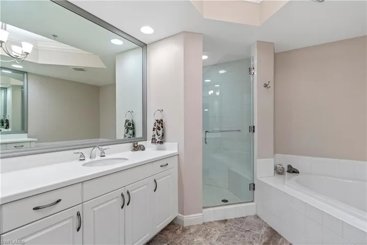Primary bathroom with dual vanities, a soaking tub, walk-in shower, and recessed lighting