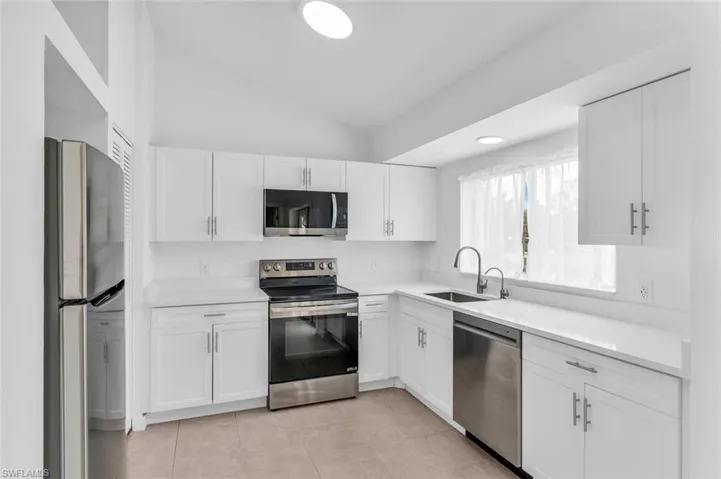 Kitchen featuring appliances with stainless steel finishes, white cabinets, light tile patterned floors, vaulted ceiling, and sink