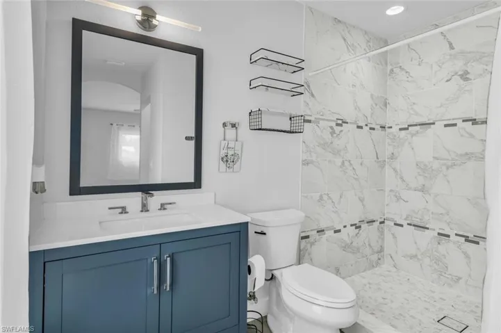 Bathroom with toilet, a tile shower, and vanity