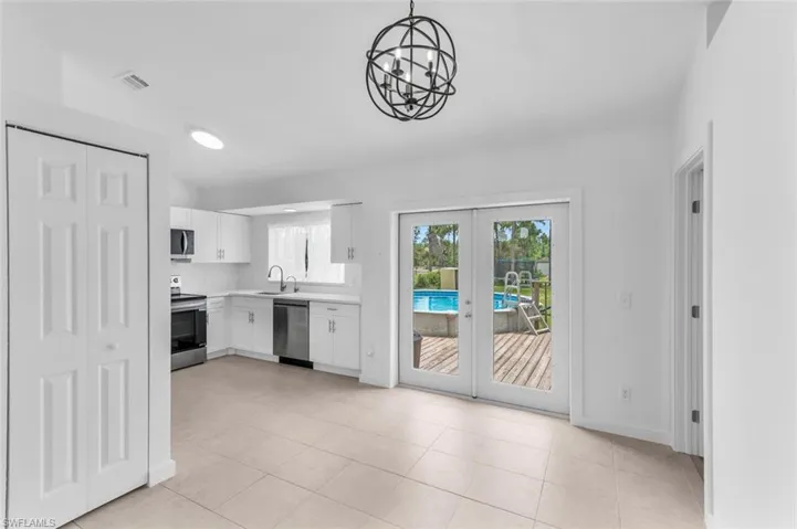 Unfurnished living room with light tile patterned flooring, french doors, sink, and an inviting chandelier