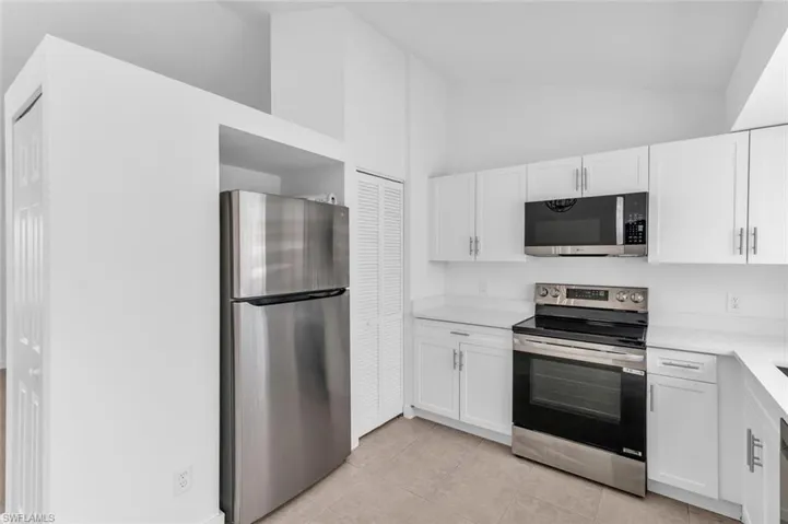 Kitchen featuring appliances with stainless steel finishes, light tile patterned flooring, high vaulted ceiling, and white cabinets