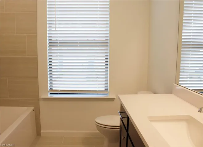 Bathroom featuring an integrated white sink, dark wood-finish vanity, and a white bathtub