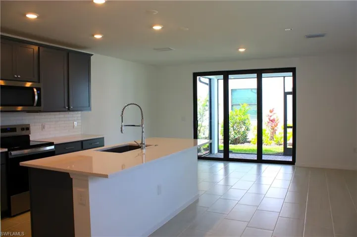 Modern kitchen featuring dark cabinetry, stainless steel appliances, a subway tile backsplash, and a large island with an undermount sink and high-arc faucet