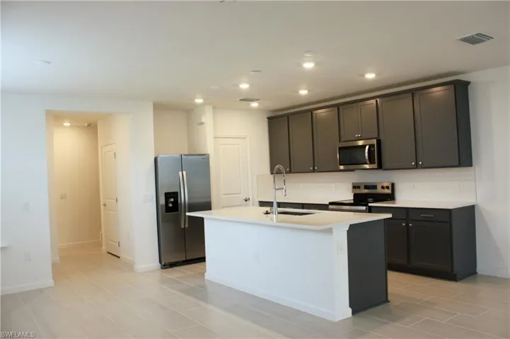 Modern kitchen featuring dark gray cabinetry, stainless steel appliances, a white subway tile backsplash, and light-colored countertops