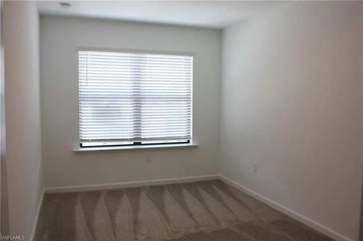 Room featuring a window with horizontal blinds, light-colored walls, and patterned carpeting